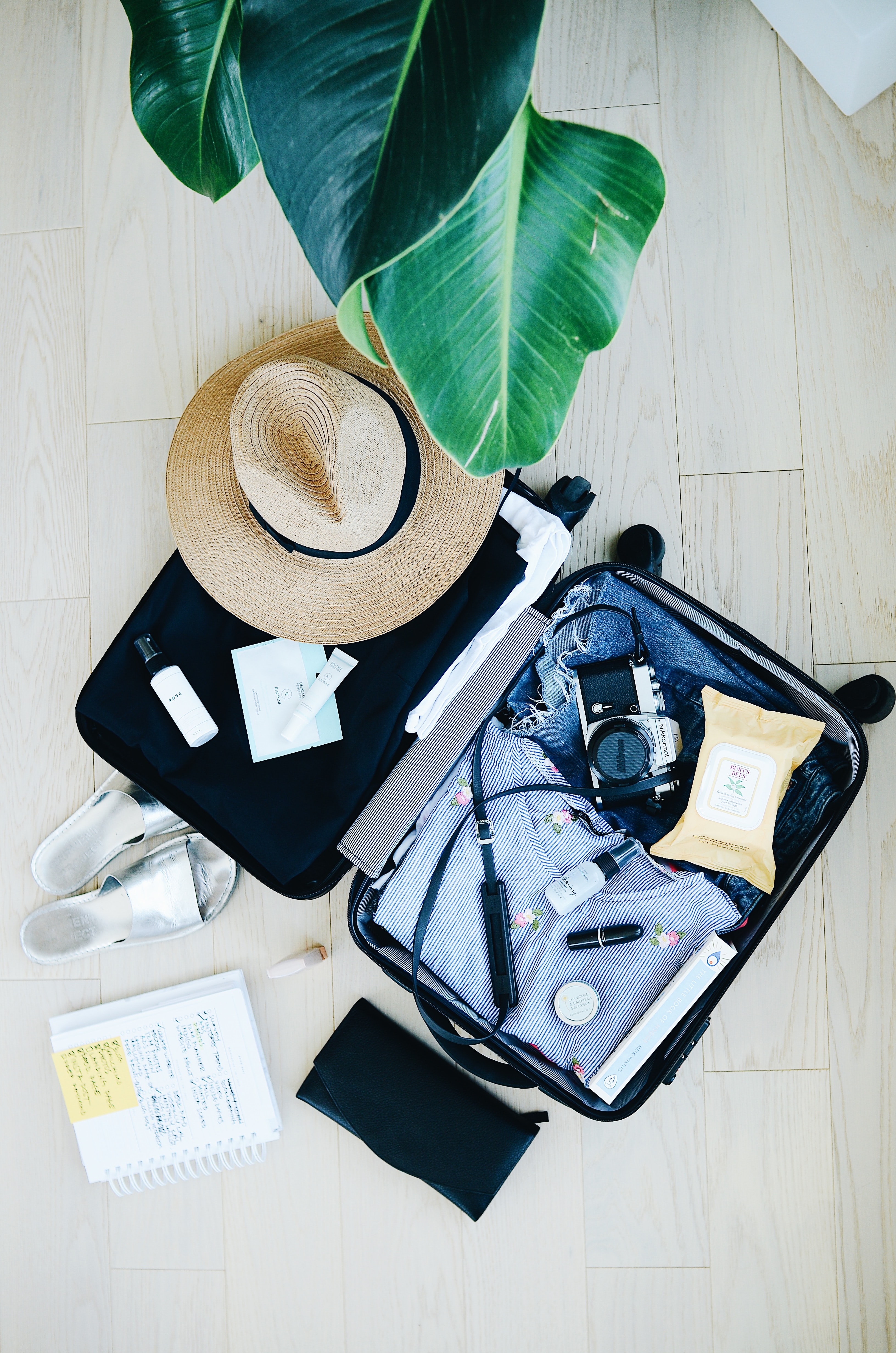 Open hand luggage case with clothes, a camera, hat, cosmetics, shoes and a notepad.