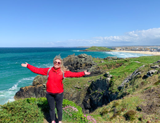 Me in a red jacket standing with arms open wide with a view of St Ives Bay in the background