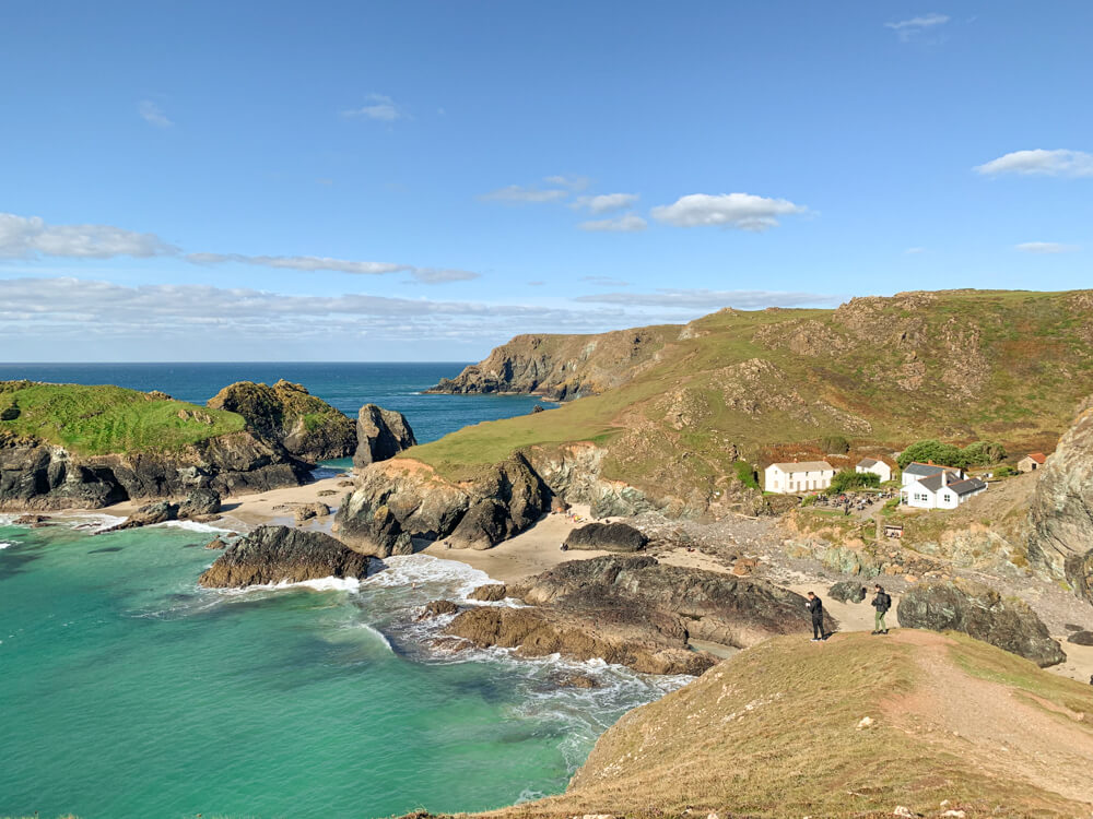 View of Kynance Cove with small white buildings on the right and the beach and ocean on the left