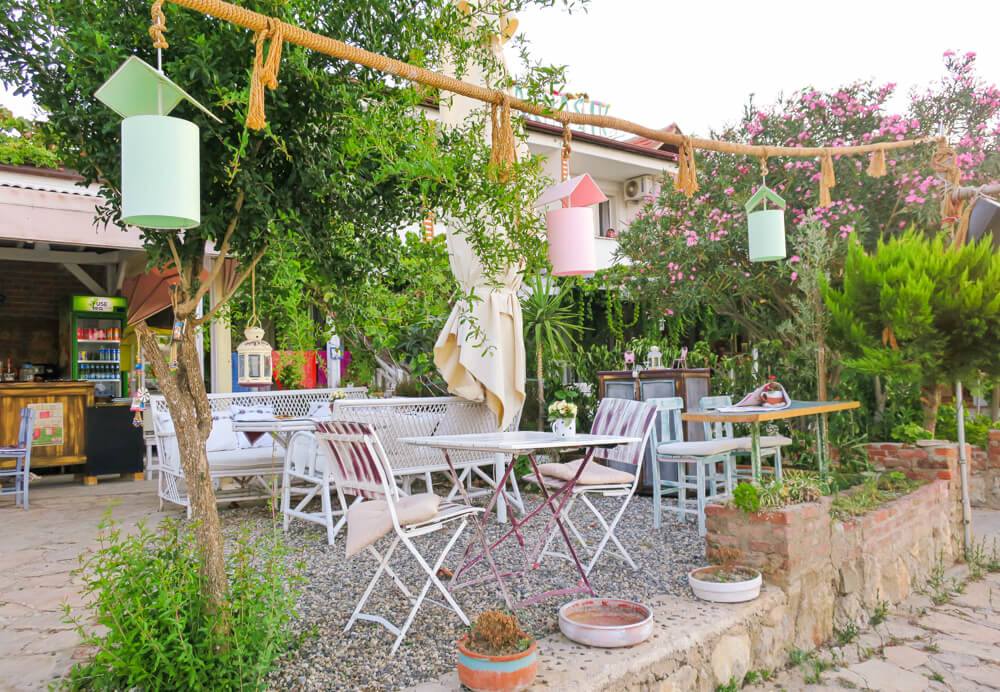 A collection of small tables with seats in Selimiye, with handing bird boxes above and trees surrounding it.