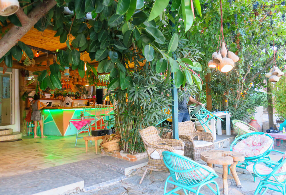 Wicker and bright blue chairs outside a colourful bar in Selimiye, with lots of trees and foliage around the entrance.