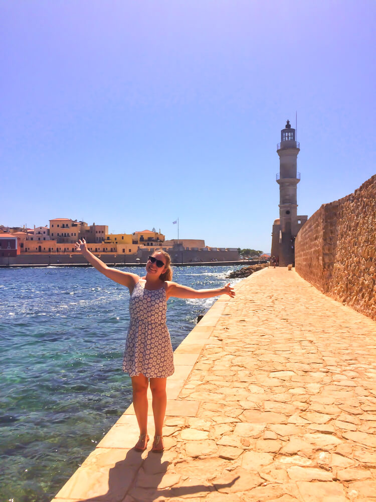 Nina (of This Planet by Nina) standing with arms open on the walkway to the old Venetian lighthouse in Chania Harbour in Crete.