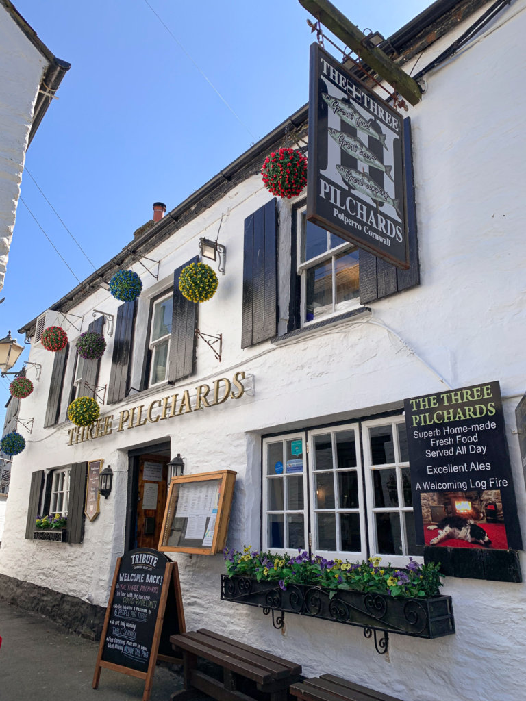 The front of the Three Pilchards pub in Polperro on the south coast of Cornwall, with colourful hanging baskets.