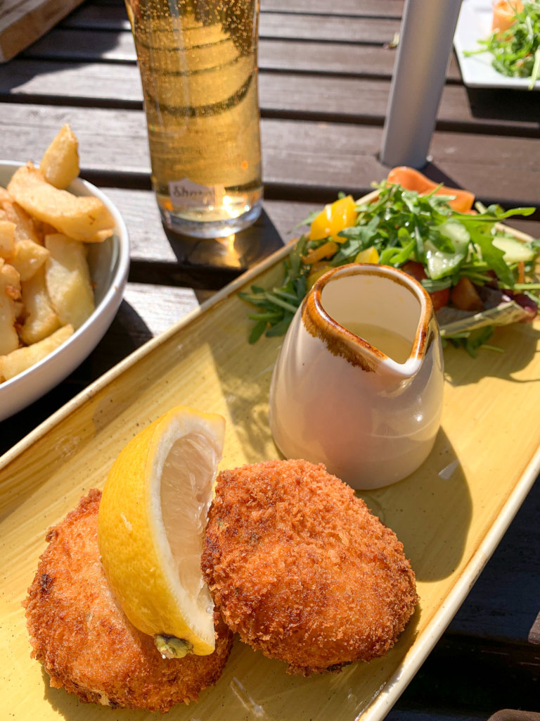 A plate of fishcakes and salad, with chips to the left and a beer at the back, at the Three Pilchards pub in Polperro on the south coast of Cornwall.