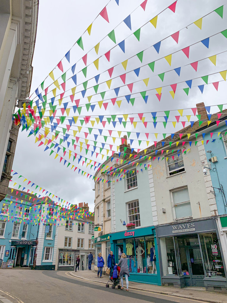 Colourful bunting hangs above Market Street in Falmouth, with blue and cream shop fronts weaving up the street.