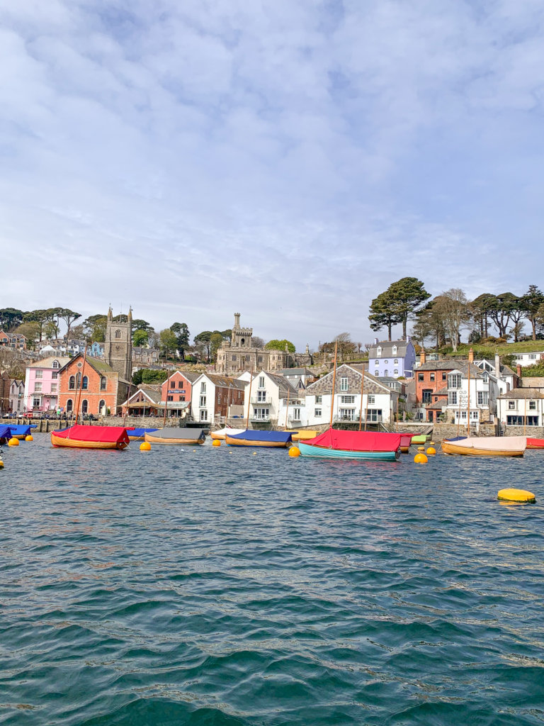 Colourful fishing boats are covered in colourful protective canvases, bobbing Fowey harbour with the town of Fowey behind them.