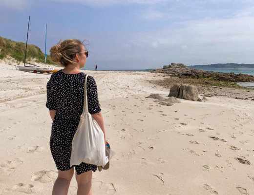 Nina wears a black polka dot dress and walks down the beach away from the camera. Blog post - Top Tips for the Isles of Scilly.