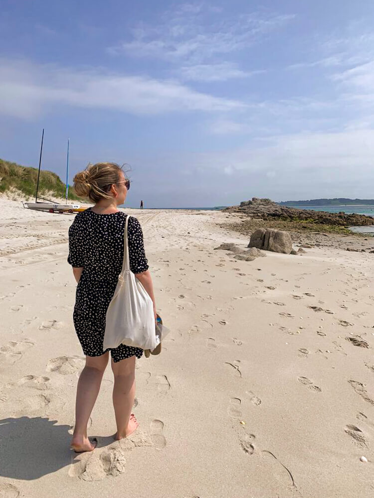 Nina wears a black polka dot dress and walks down the beach away from the camera. Blog post - Top Tips for the Isles of Scilly.