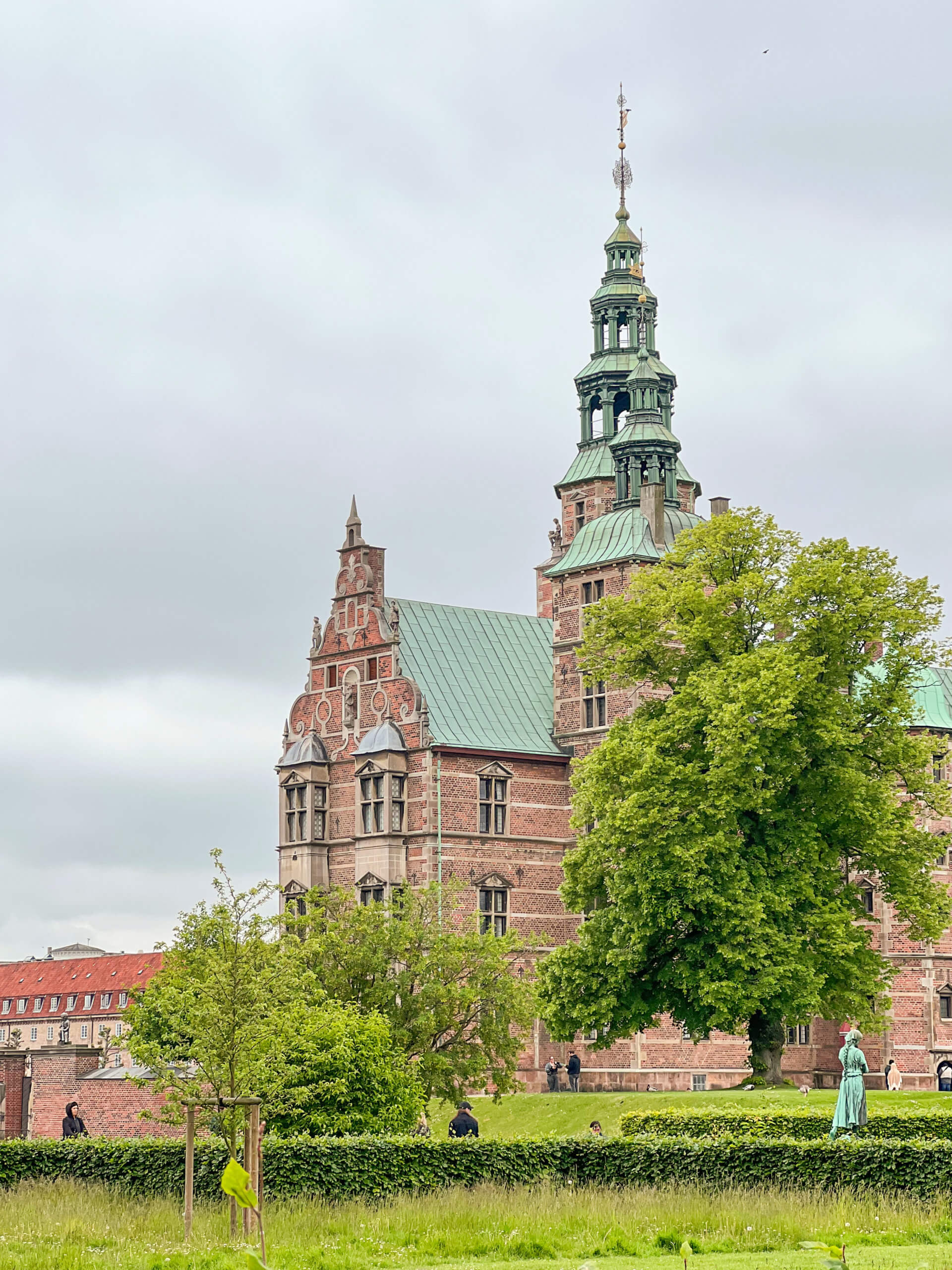 Rosenborg Castle partially obstructed by trees, with its ornate green turrets reaching up to the sky. One of my top 10 places to visit in Copenhagen.