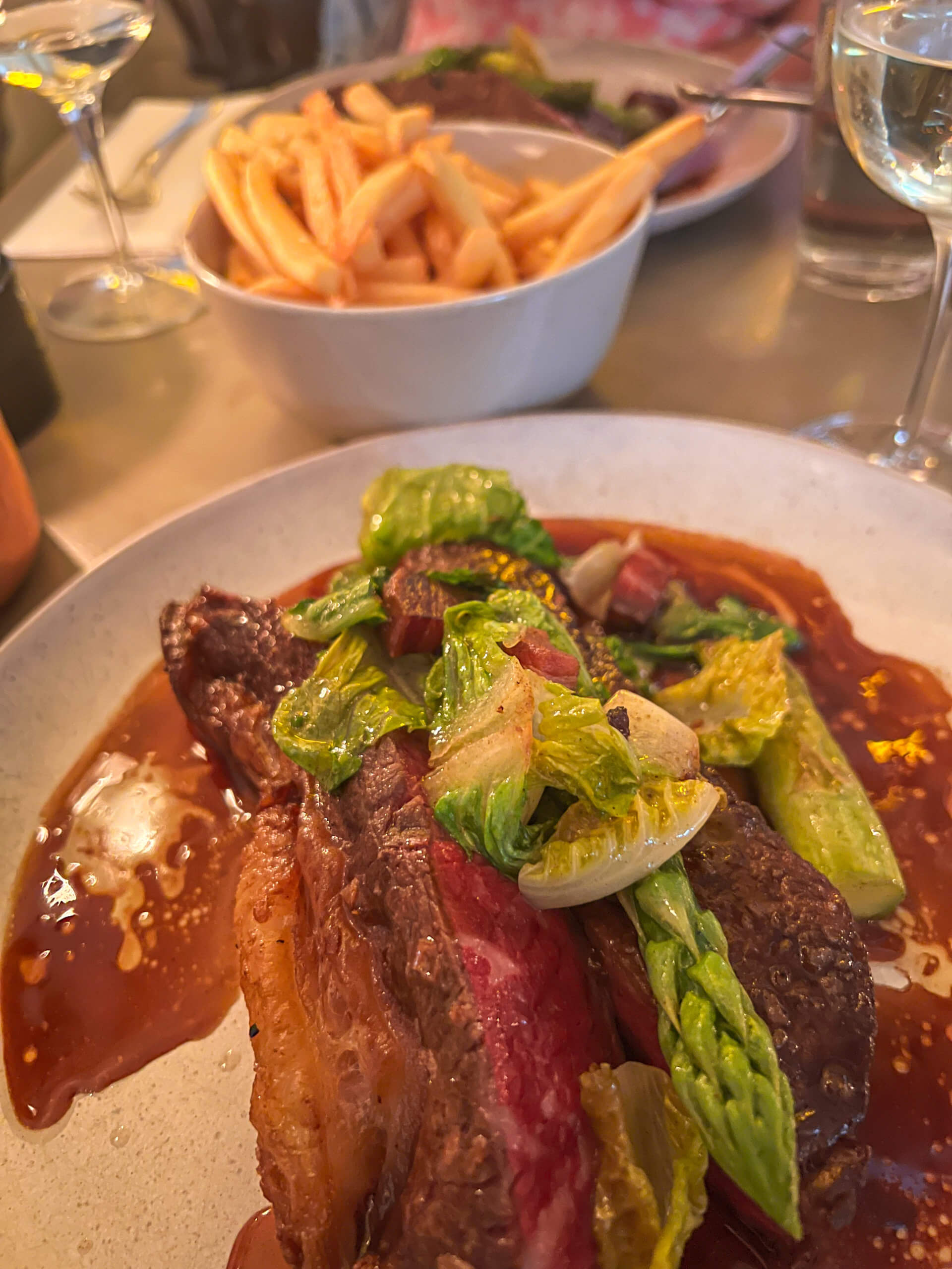 Close up of a steak dish with asparagus on top, with a bowl of fries in the background. One of my top 10 places to visit in Copenhagen.