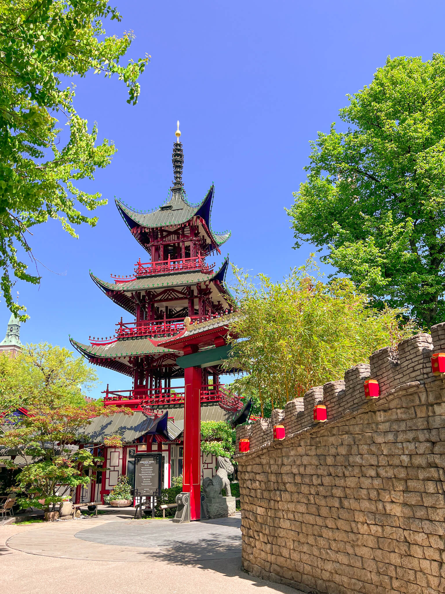 A red and green Chinese tower structure juts out from the trees at Tivoli Gardens. One of my top 10 places to visit in Copenhagen.