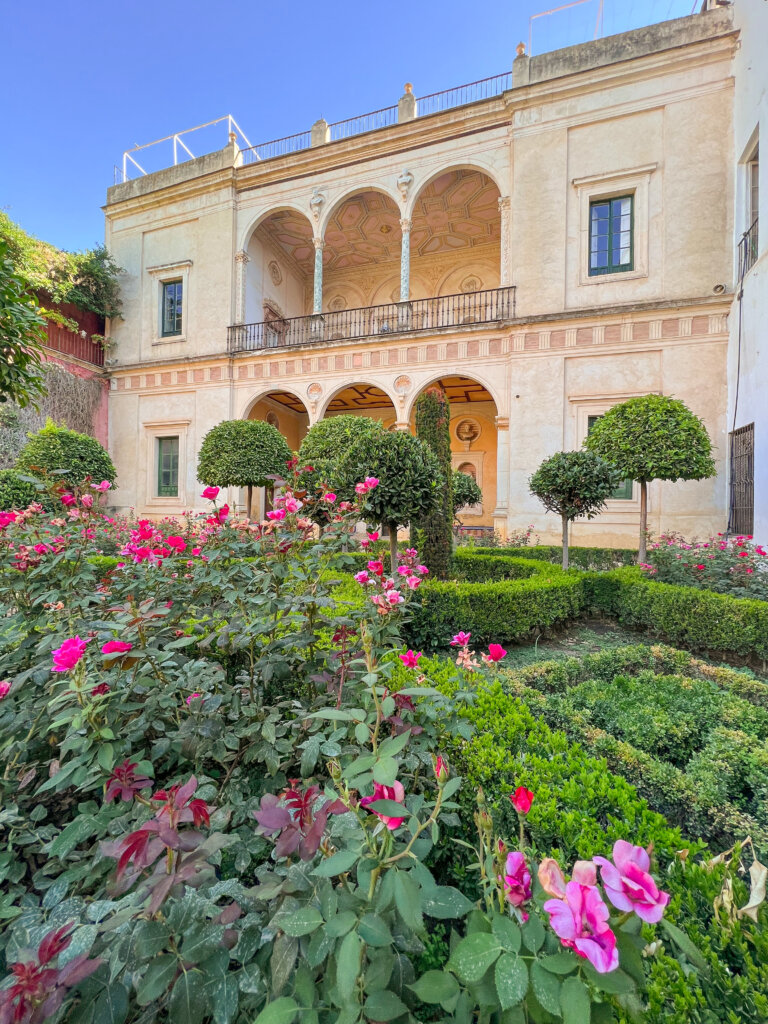 View across green foliage with pink flowers to the Casa de Pilatos - 10 things to do in Seville